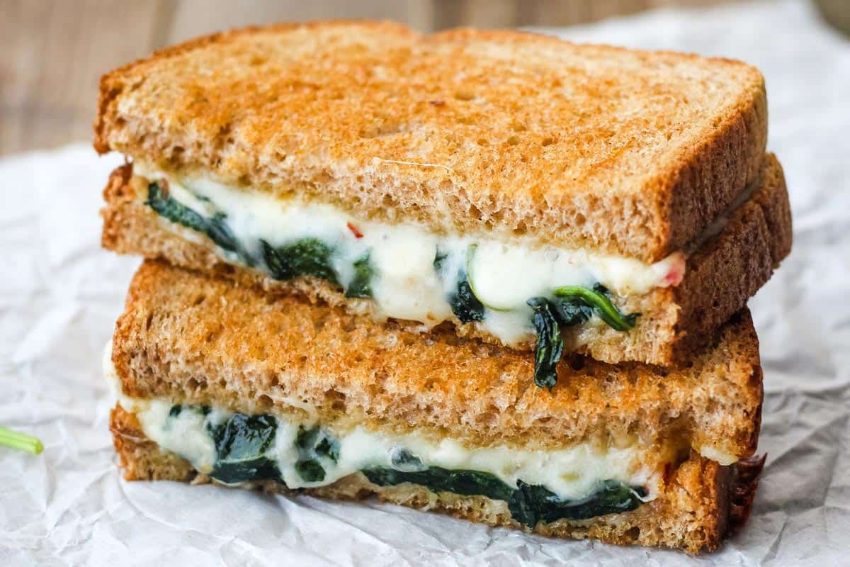 Closeup of gooey melted cheese and spinach inside a baked grilled cheese sandwich.