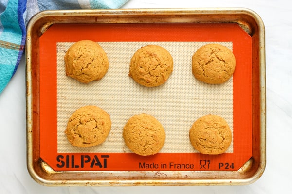 Six baked cookies cooling on a lined pan.