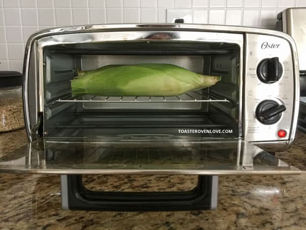 Corn on the cob baking side of a small toaster oven.