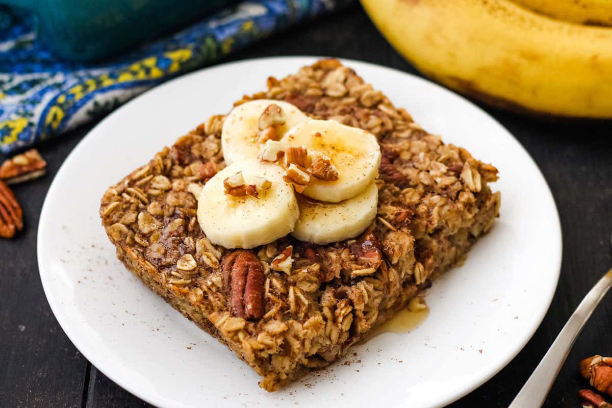 Baked oatmeal on plate topped with banana slice and drizzle of maple syrup.
