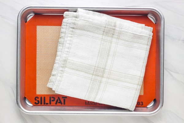 Quarter sheet pan lined with a silicone baking mat and a folded flour sack towel.