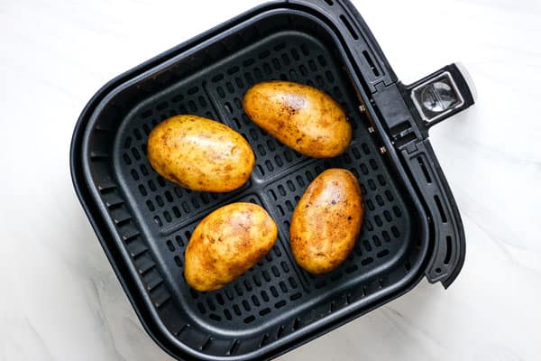 Oiled potatoes in an air fryer basket.
