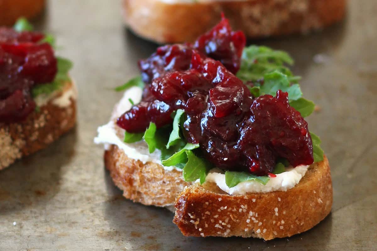 Closeup of crostini topped with goat cheese, arugula, and balsamic roasted cranberries.