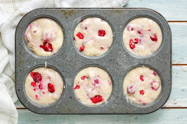 Overhead view of raspberry muffin batter in oiled tin.