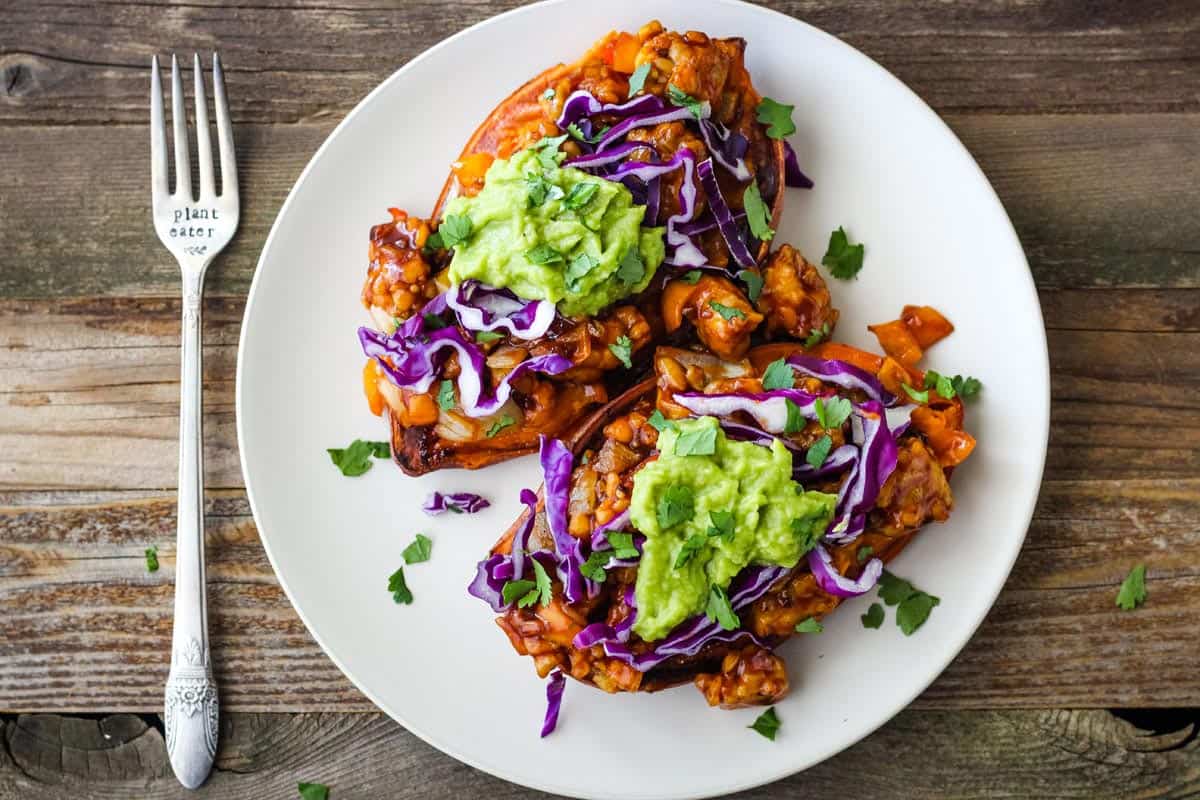 Overhead view of stuffed sweet potatoes on plate with fork stamped "plant eater."