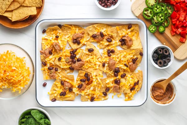 Rimmed pan with chips topped with beans and shredded cheese.