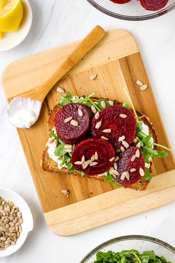 Toasted bread on a cutting board topped with sliced beetroot and cottage cheese.