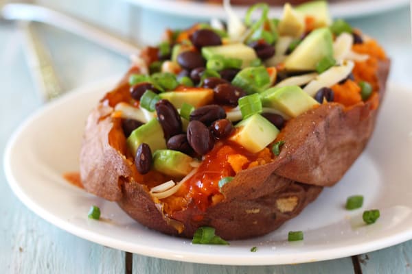 Closeup of a loaded sweet potato drizzled with hot sauce.