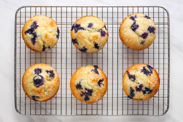 Overhead view of six blueberry muffins on a cooling rack.