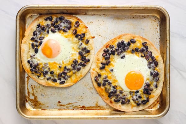 Overhead view of crispy tostadas with baked eggs and black beans.