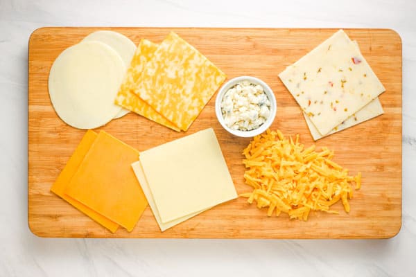 Cutting board with a variety sliced, grated, and crumbled cheeses.