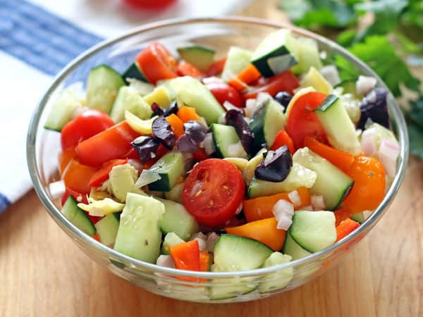 A small bowl of chopped vegetables next to a pile of parsley.