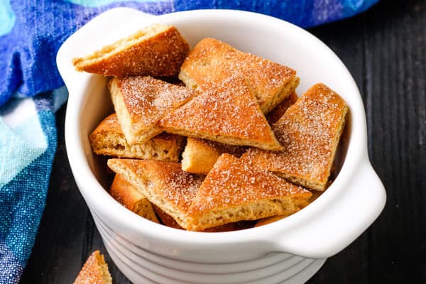Small cinnamon sugar pita triangles in a ramekin on a table.