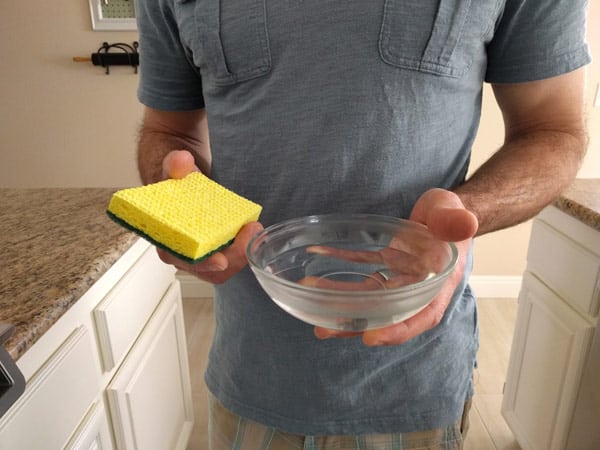 Man holding a yellow sponge and bowl of warm water.