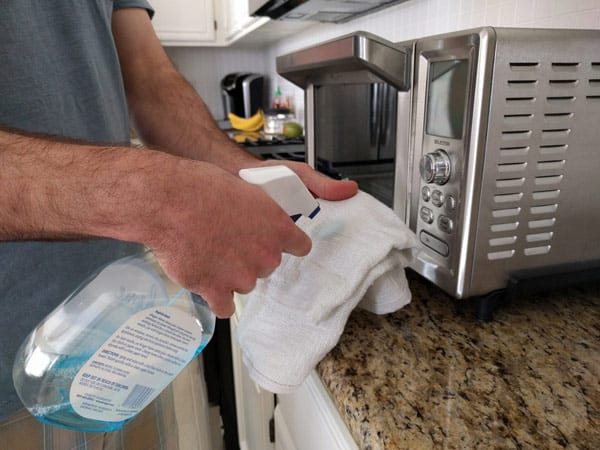 Man spraying cleaner onto a white rag in front of a toaster oven.