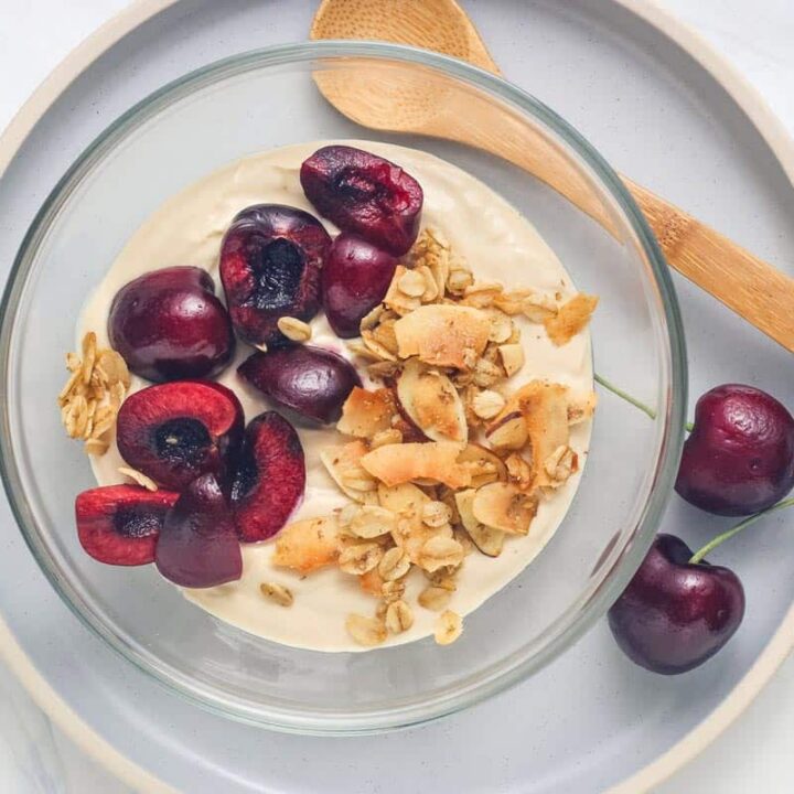 Small bowl of coffee Greek yogurt topped with chopped fresh cherries and flaky granola.