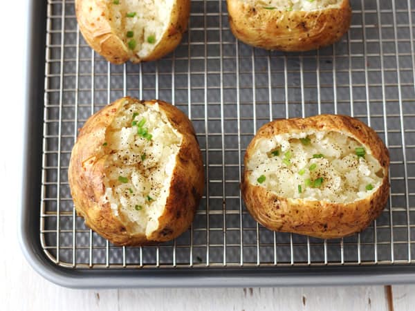 Overhead view of baked potatoes opened, fluffed, and topped with chives.