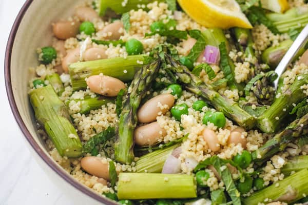 Closeup of beans, peas, asparagus, and mint in a bowl with a fork.