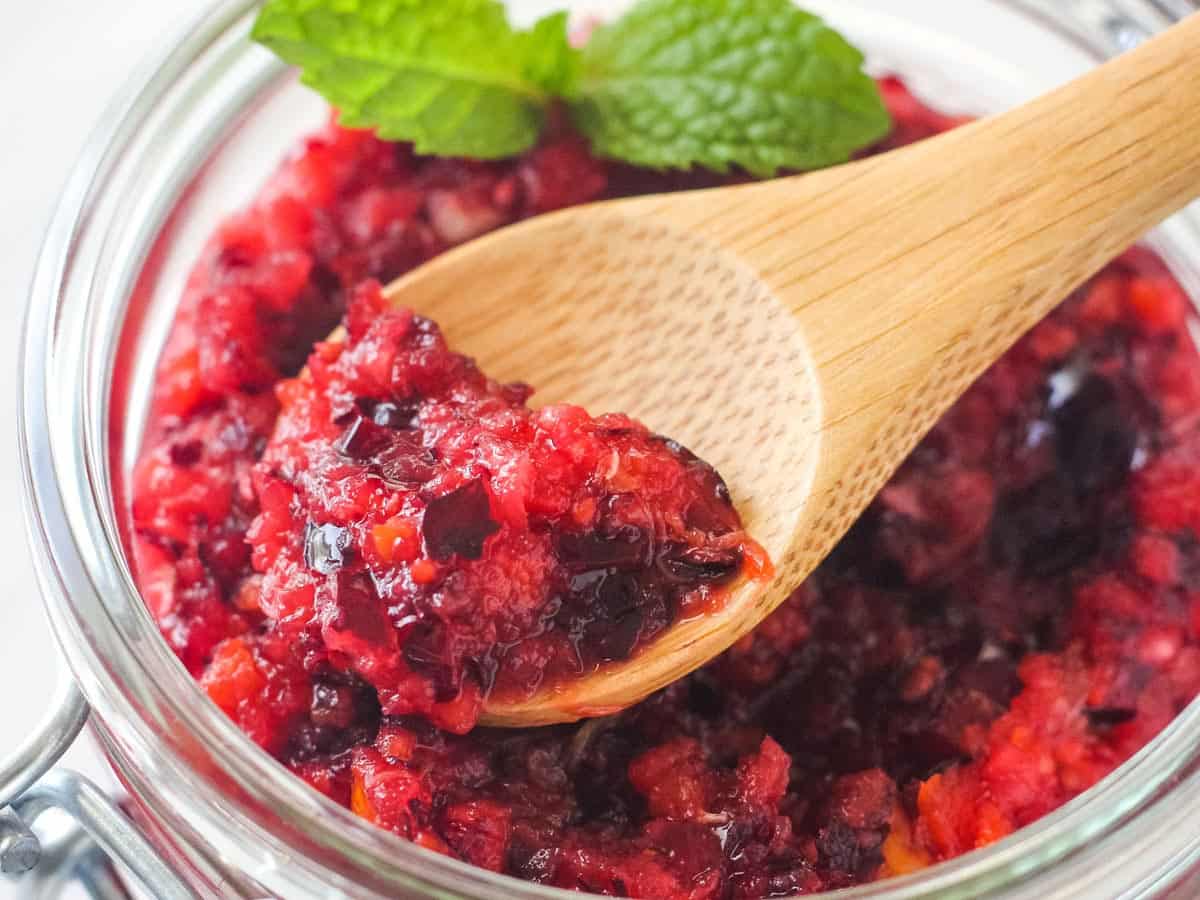 Closeup of spoon scooping a chunky cranberry relish from a mason jar.