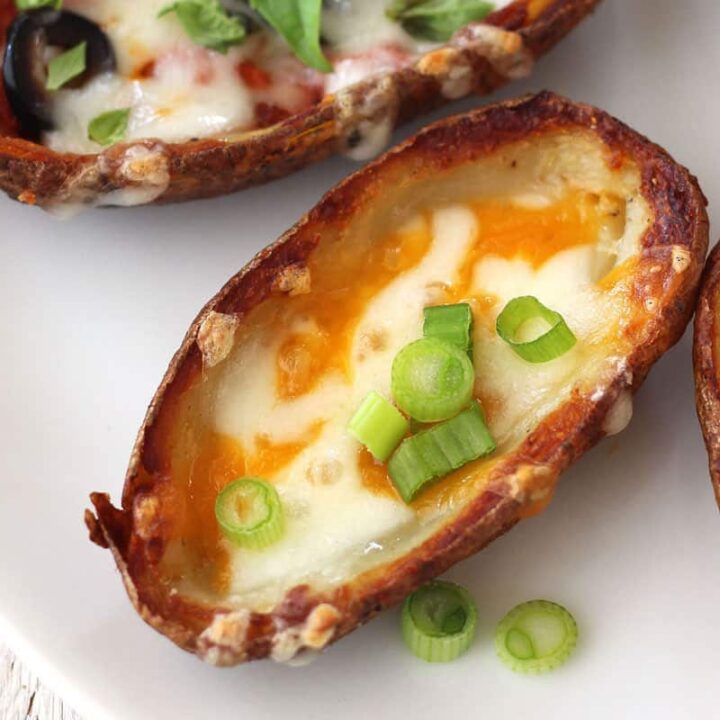Closeup of crispy baked potato skin with melted cheese and green onion slices on a plate.