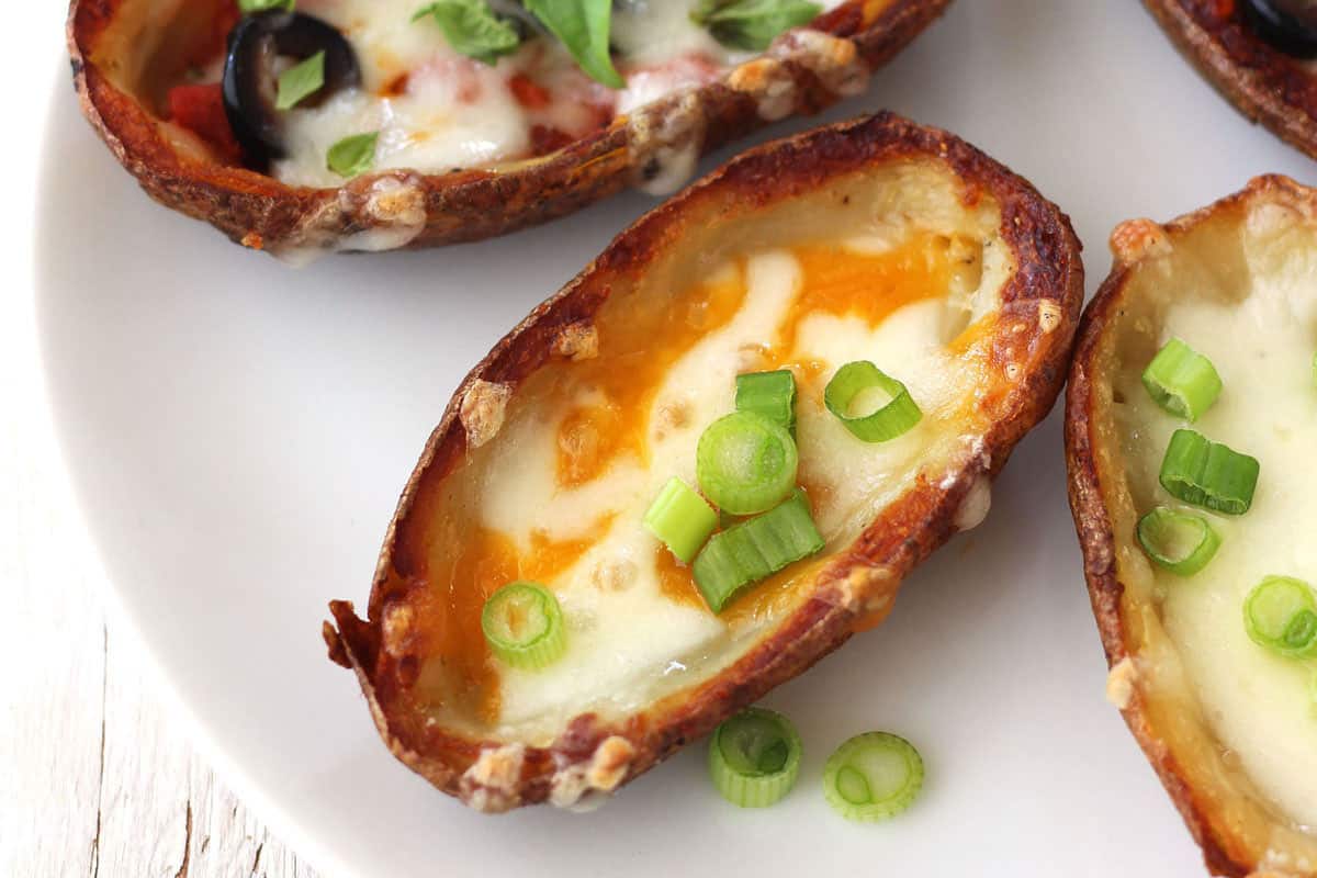 Closeup of crispy baked potato skin with melted cheese and green onion slices on a plate.