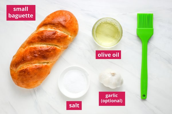 Mini bread loaf, ramekins of oil and salt, and a head of garlic labeled on a table.