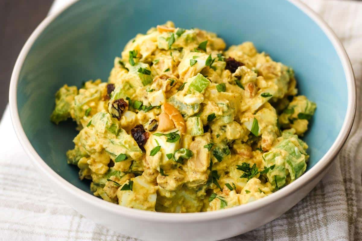 Closeup of bowl of egg salad with chopped celery, raisins, and cashews.
