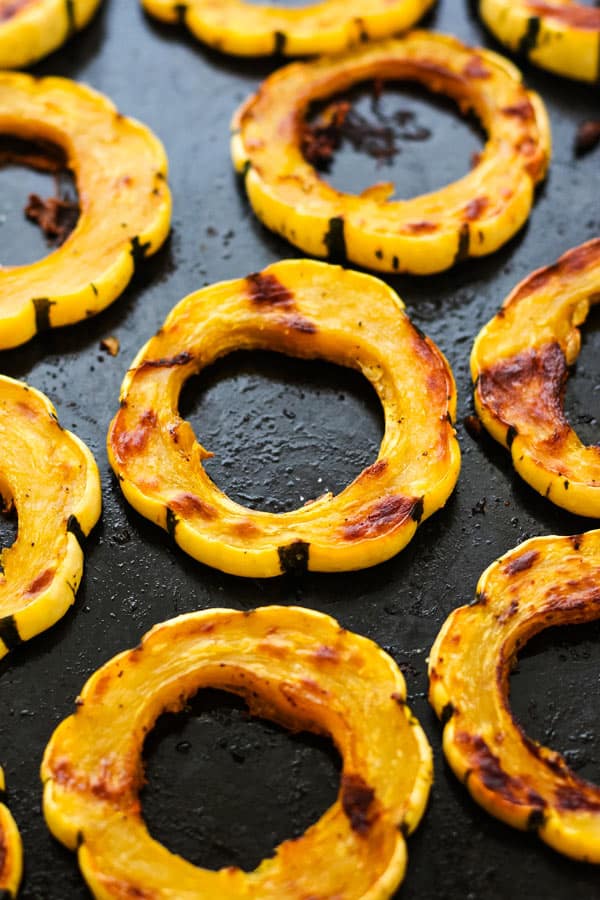 Cooked delicata squash slices on a roasted pan.
