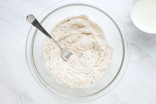 Glass bowl with flour and seeds mixed with a fork.