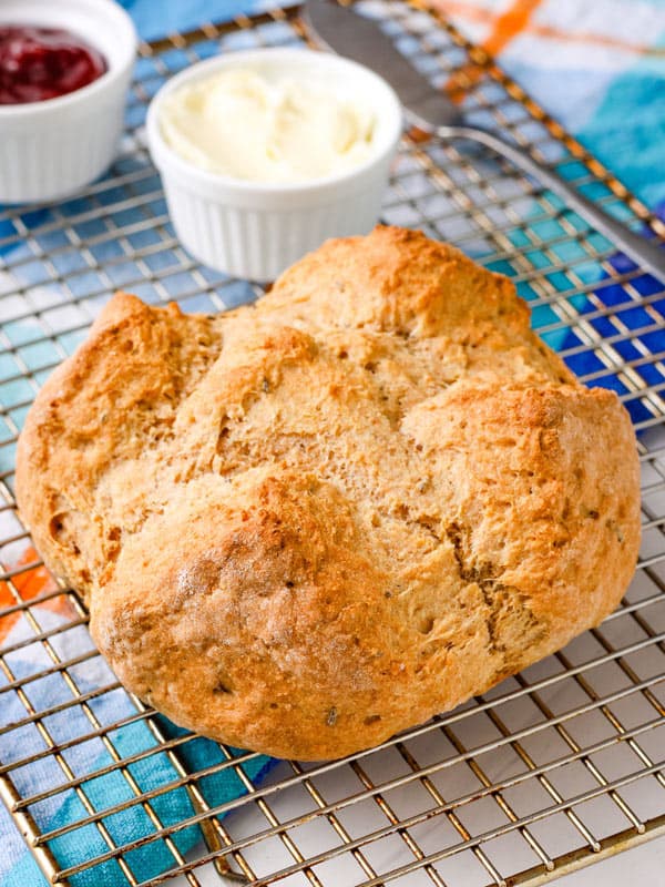Small baked soda bread on a cooling rack with butter and jam.