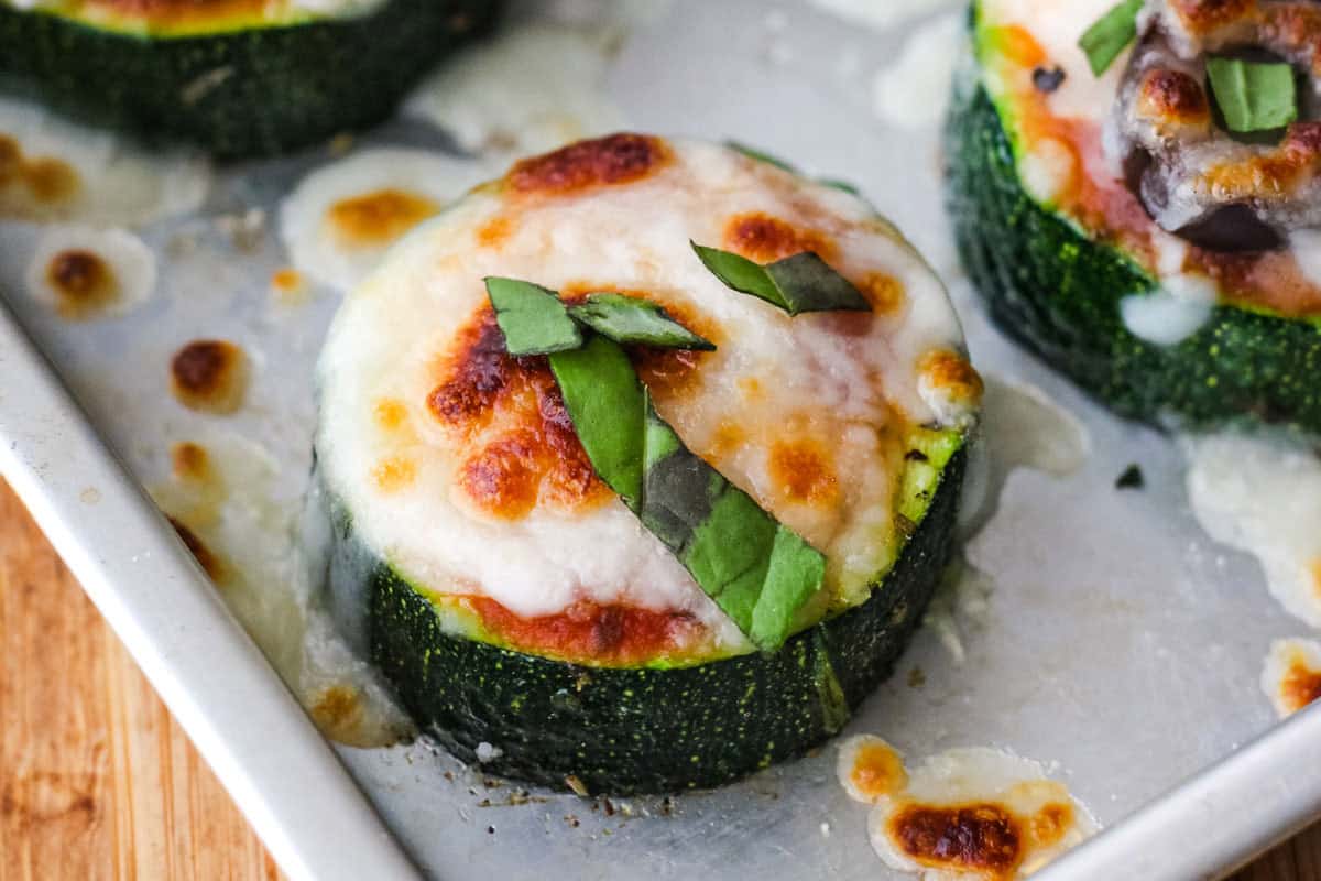 Closeup of a mini zucchini pizza with melted cheese and fresh basil.