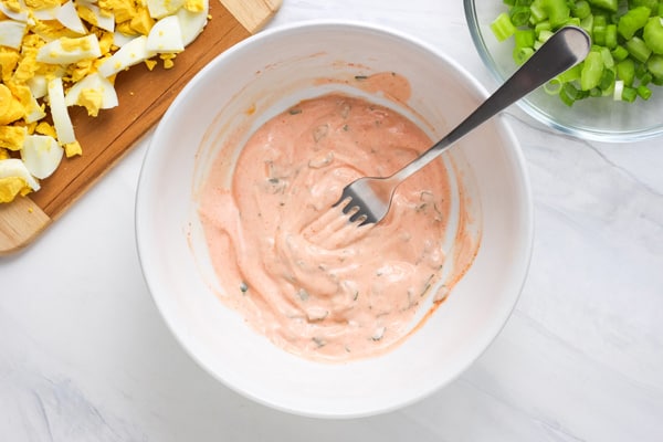 Fork mixing yogurt and sriracha in a bowl.