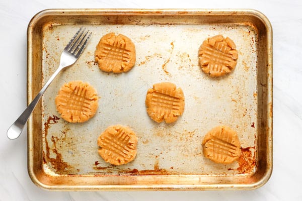 Flattened cookie dough on a sheet pan with a fork.
