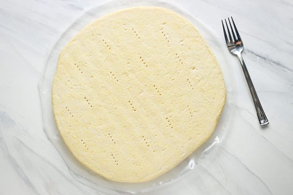 Frozen pizza crust with holes poked in it next to a fork.