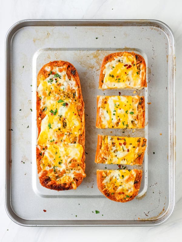Overhead view of cheesy garlic bread sliced into pieces on a pan.