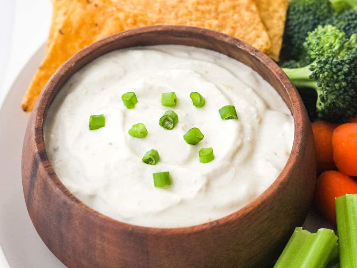 Small wooden bowl filled with dip and topped with sliced green onion.
