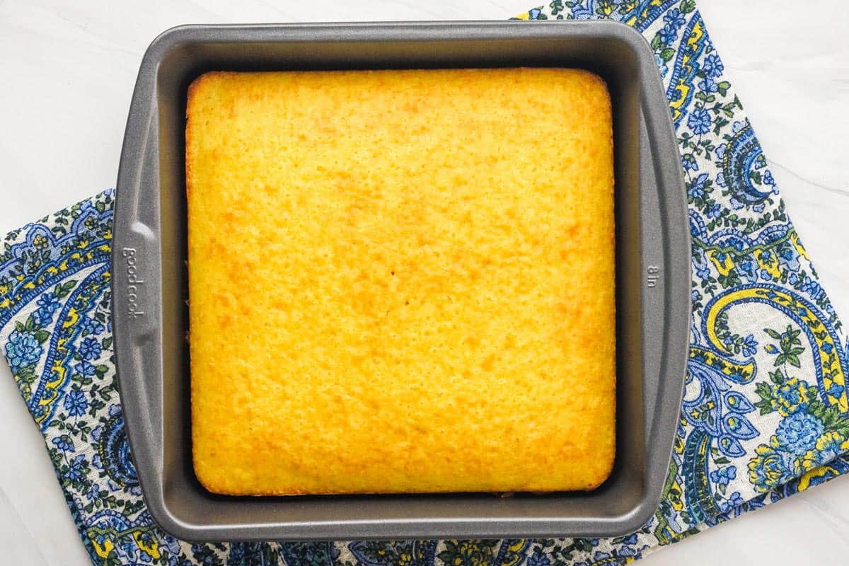 Overhead view of yellow cake in an 8x8 metal pan on a paisley napkin.