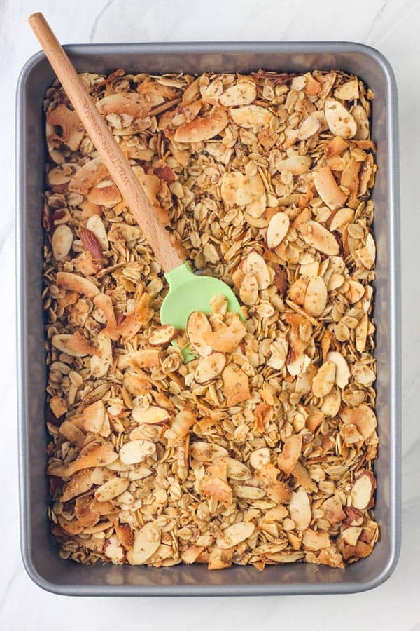 Overhead view of a small pan with golden toasted granola stirred with a rubber spatula.