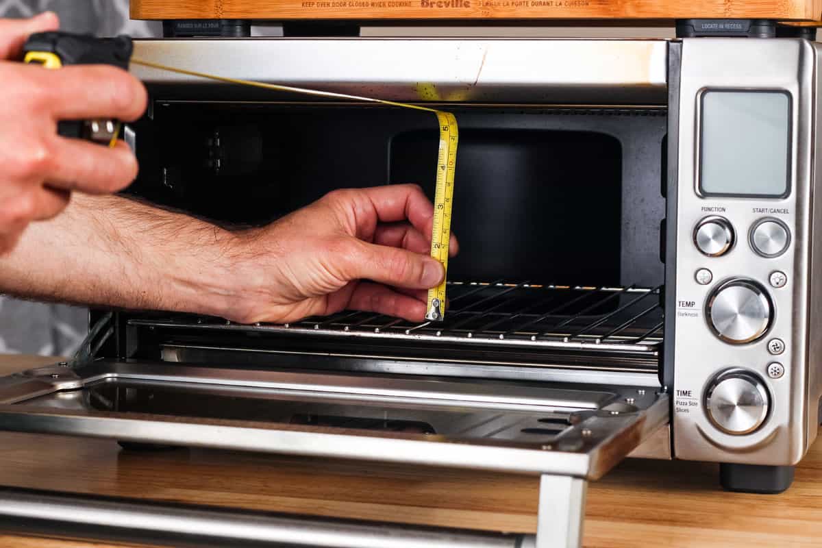 Hand holding tape measure from bottom rack to the roof of a toaster oven.