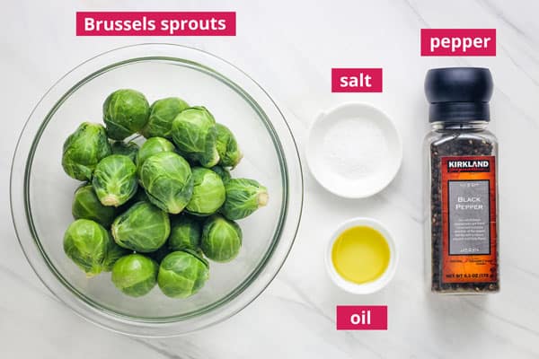 Bowl of whole Brussels sprouts, pepper grinder, and ramekins with salt and olive oil.