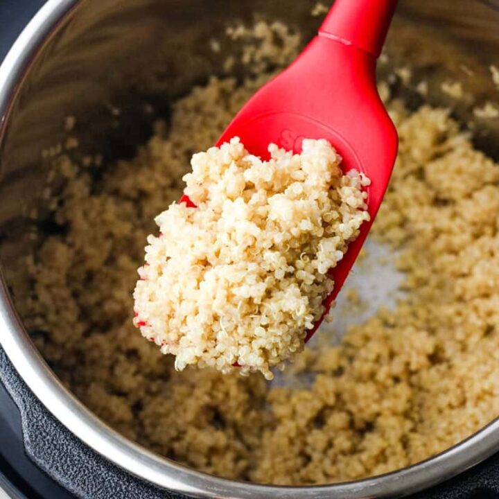 Red silicone spatula with scoop of cooked quinoa over an instant pot.