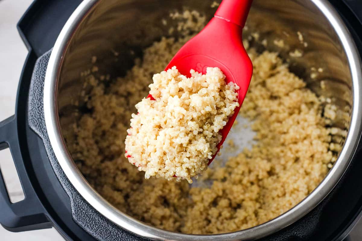 Red silicone spatula with scoop of cooked quinoa over an instant pot.
