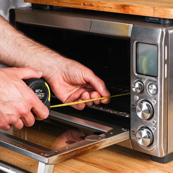Hands holding tape measure inside a toaster oven.