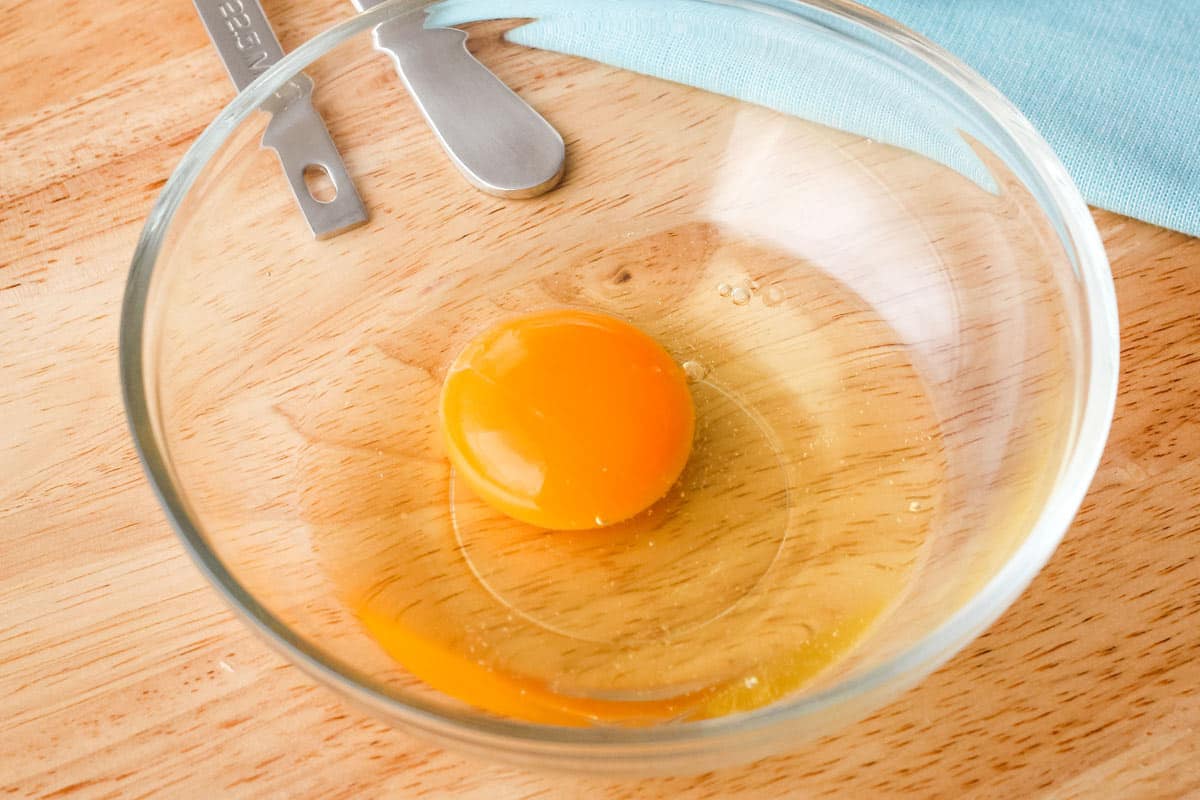 Large egg in a small glass bowl next to measuring spoons.