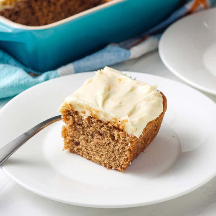 Small blue baking dish and plates with pieces of frosted spice cake on a table.
