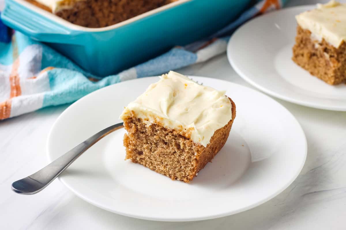 Small blue baking dish and plates with pieces of frosted spice cake on a table.
