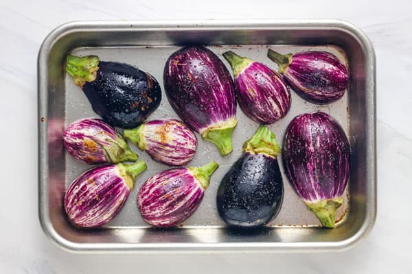 Vibrant purple eggplant halves on a small eighth sheet pan.