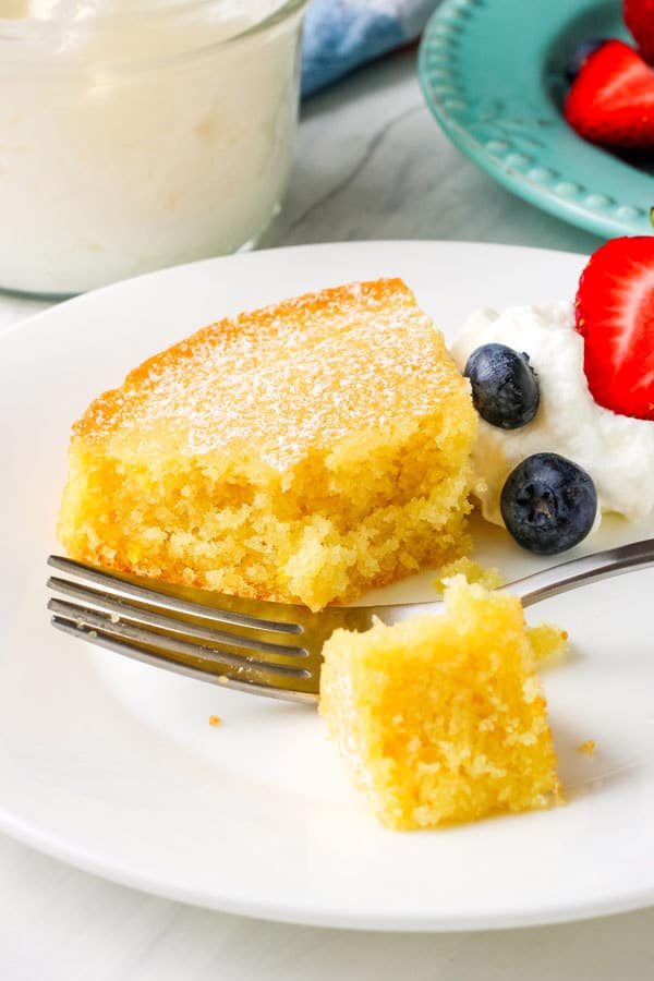 Closeup of tender cake slice on plate with blueberries and whipped cream.