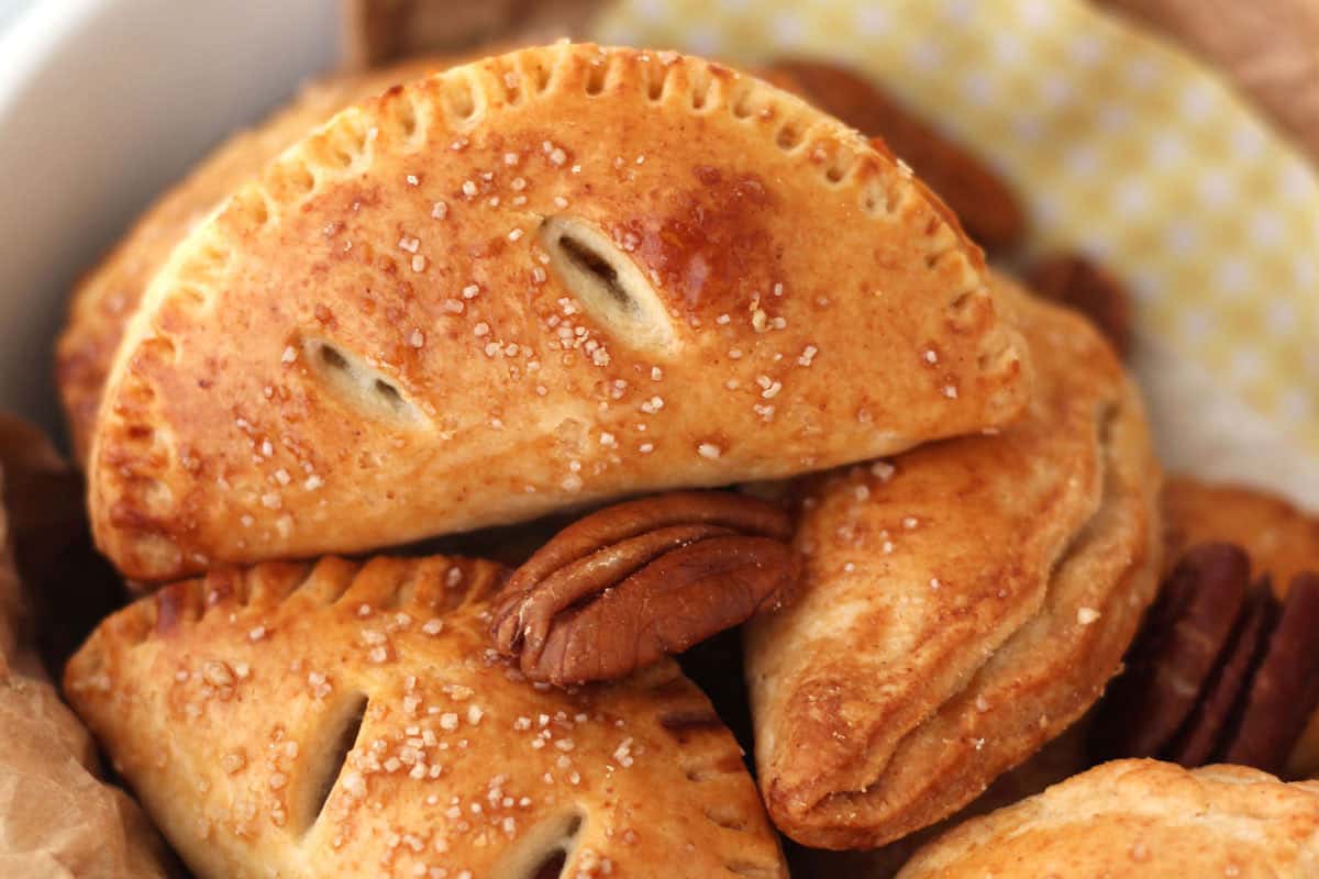 Closeup of golden brown mini hand pies and whole pecans in a bowl.