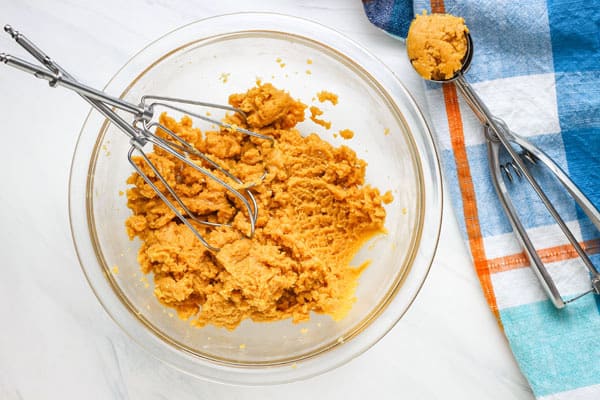Cookie dough in a glass bowl and in a metal cookie scoop.